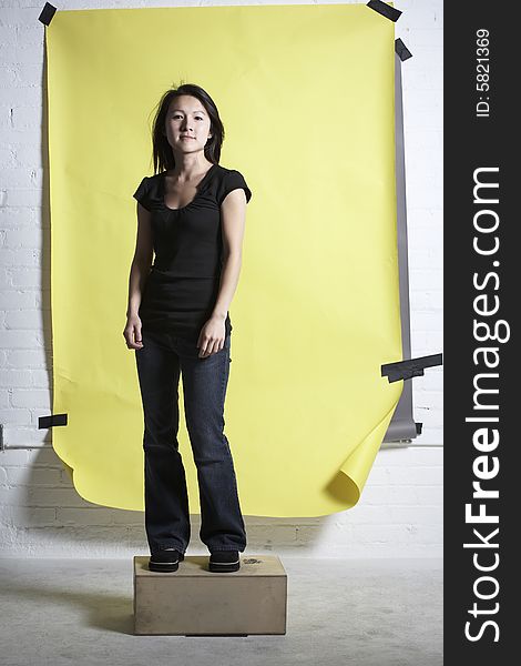 Young Asain woman wearing a back top and denm pants stands in front of a yellow paper background. Young Asain woman wearing a back top and denm pants stands in front of a yellow paper background.