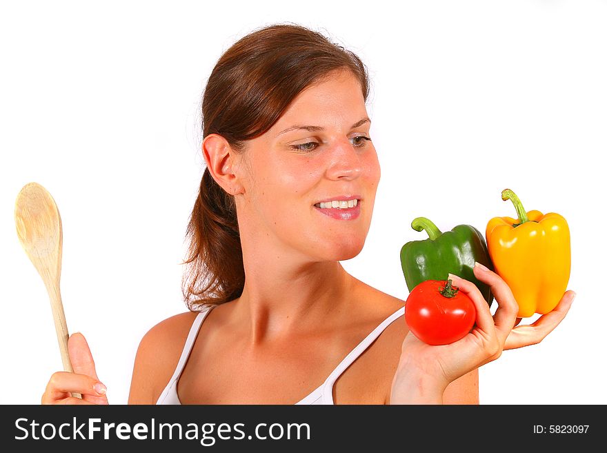 A young woman with vegetables in one hand and a wooden spoon in the other. A young woman with vegetables in one hand and a wooden spoon in the other.