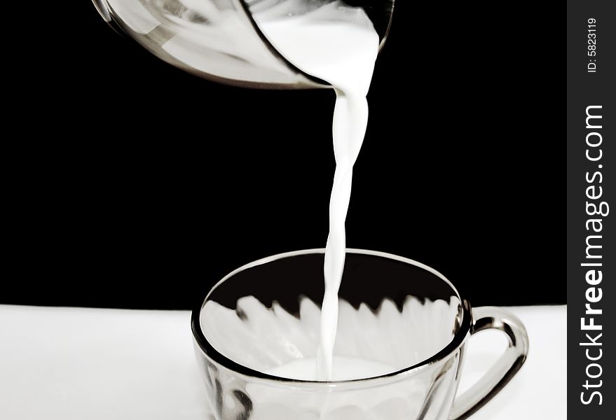 The milk flowing in a mug, isolated on black background.