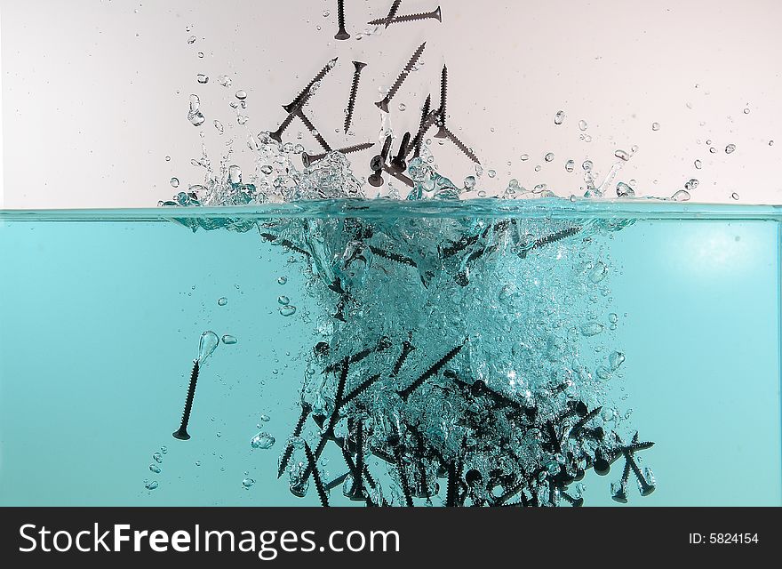 A group of black screws drop into water. A group of black screws drop into water