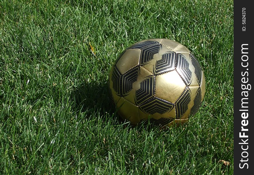 A gold soccer ball left on the grass.