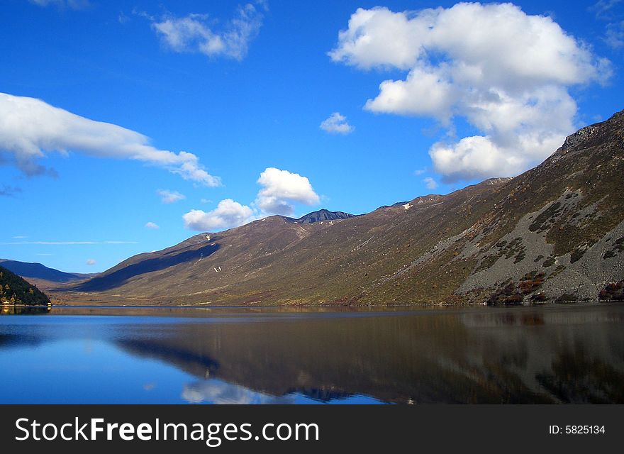 A quiet lake with white clouds floated in the sky.A mountain adjacent to the lake.Mugecuo Lake ,Kangding,Sichuan,China. A quiet lake with white clouds floated in the sky.A mountain adjacent to the lake.Mugecuo Lake ,Kangding,Sichuan,China