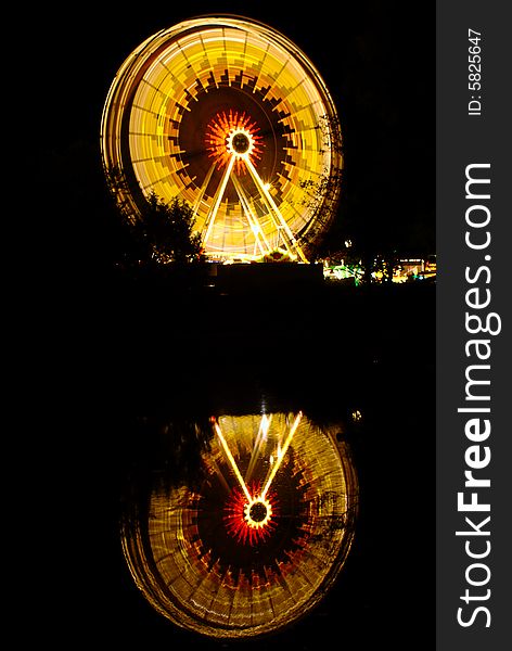 Ferris wheel at night at Ulm's folk festival with its reflection on a water surface.