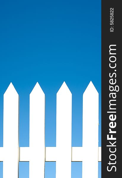 A white picket fence background in front of a bright blue sky with copy space.
