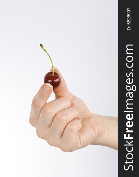 Red cherry is in the hand, between fingers. Red cherry is in the hand, between fingers