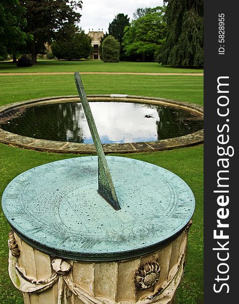 A classic sundial in front of a circular pond in a beautiful garden. A classic sundial in front of a circular pond in a beautiful garden