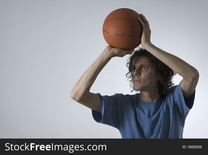 A young man aiming to shoot a basketball.  He is staring intensely ahead.  Horizontally framed shot. A young man aiming to shoot a basketball.  He is staring intensely ahead.  Horizontally framed shot.