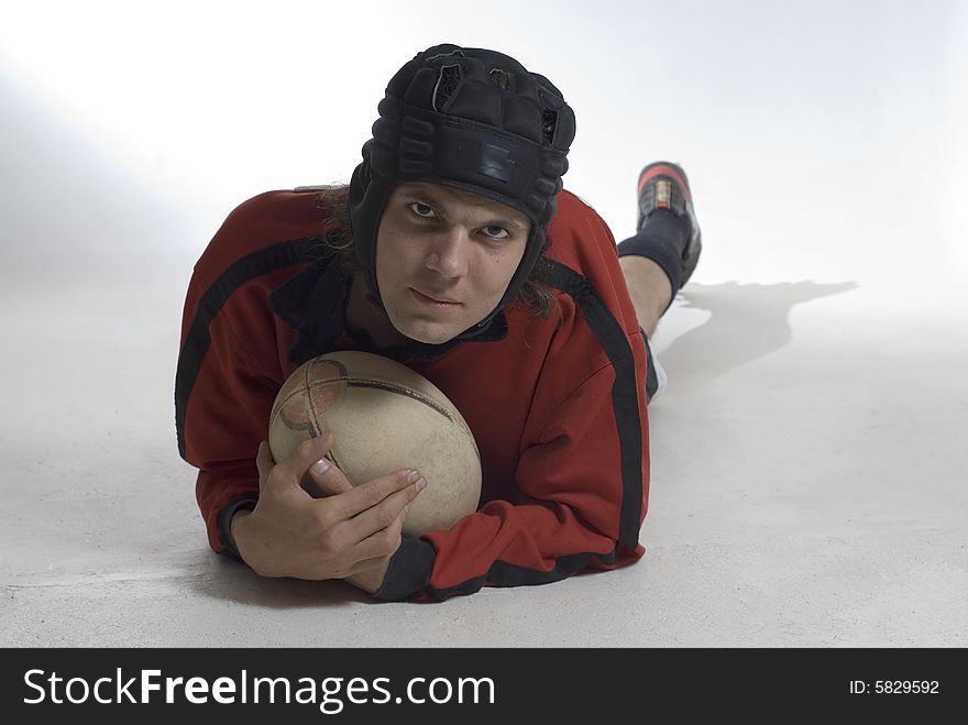 Man wearing a helmet holds a rugby football and lies on the floor.  Horizontally framed photograph. Man wearing a helmet holds a rugby football and lies on the floor.  Horizontally framed photograph