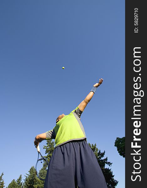 A man is standing outside on a tennis court. He is holding a tennis racket, about to hit the tennis ball, and looking away from the camera. A man is standing outside on a tennis court. He is holding a tennis racket, about to hit the tennis ball, and looking away from the camera.