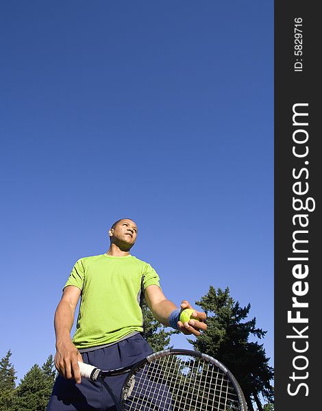 A man is standing outside on a tennis court.  He is holding a tennis racket and ball, and looking away from the camera. A man is standing outside on a tennis court.  He is holding a tennis racket and ball, and looking away from the camera.