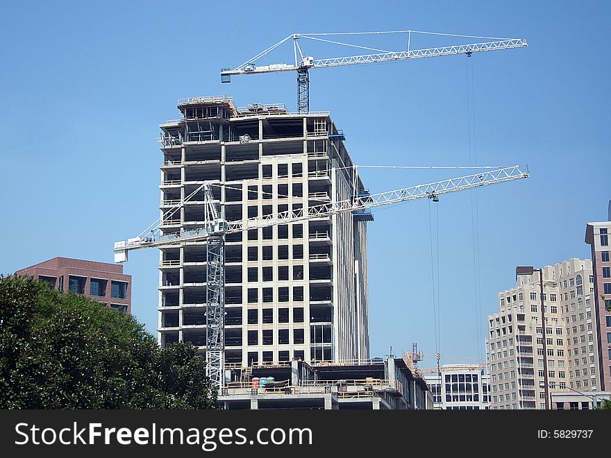 Two cranes are in the foreground of the construcion of a large building. Two cranes are in the foreground of the construcion of a large building