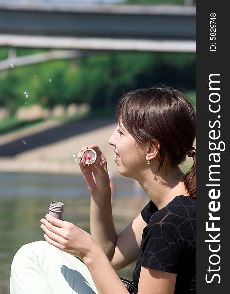 The young girl is amused that inflates soap bubbles on coast of the river. A photo on a theme of carefree summer holiday.