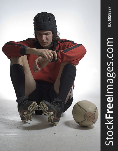 Rugby player sitting with his elbows on his knees looking sad with his football by his side. Vertically framed photograph. Rugby player sitting with his elbows on his knees looking sad with his football by his side. Vertically framed photograph