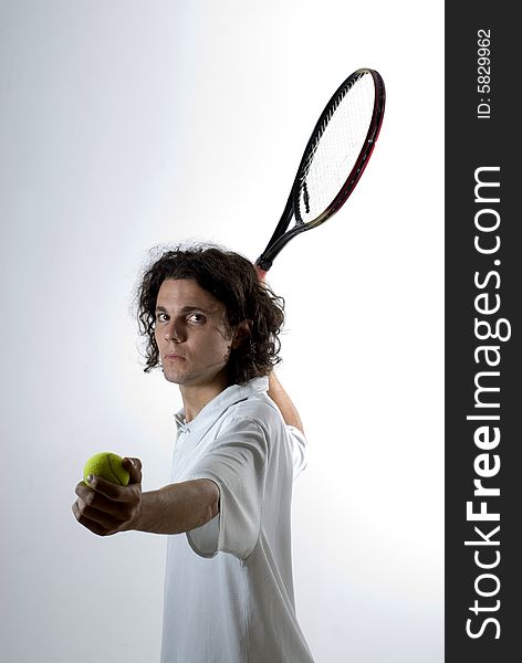 A young man, holds a tennis racket back and a ball forward, getting ready to serve the ball. He stares at the camera. Vertically framed shot. A young man, holds a tennis racket back and a ball forward, getting ready to serve the ball. He stares at the camera. Vertically framed shot.