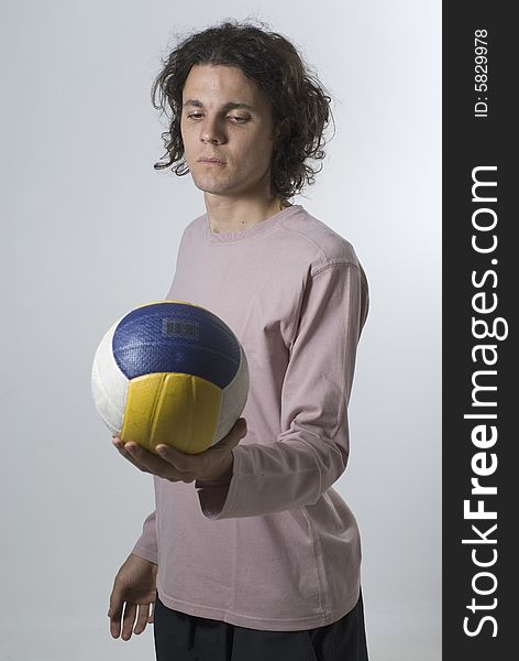 Man holds a volleyball and stares at it with a serious expression on his face.  Vertically framed photograph. Man holds a volleyball and stares at it with a serious expression on his face.  Vertically framed photograph