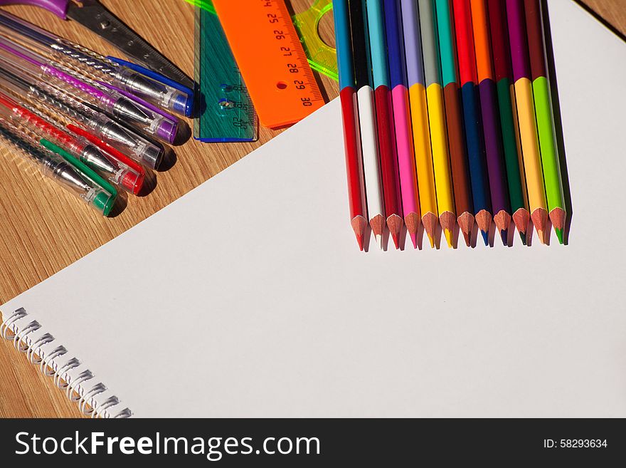 Colored pencils, pens, rulers with a white notebook on the wooden table. Colored pencils, pens, rulers with a white notebook on the wooden table