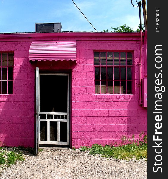 A view of the front of a bright pink building.  There is a door and windows.  Vertically framed shot. A view of the front of a bright pink building.  There is a door and windows.  Vertically framed shot.