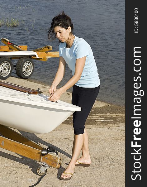 A young woman is  fixing something on her sailboat.  She is looking at the ropes in her hands.  Vertically framed shot. A young woman is  fixing something on her sailboat.  She is looking at the ropes in her hands.  Vertically framed shot.