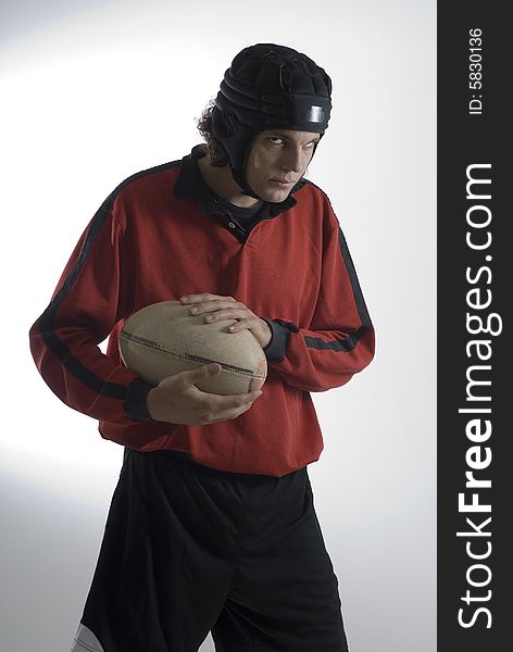 Rugby player wearing a helmet and uniform holds a football and has a sullen look on his face. Vertically framed photograph. Rugby player wearing a helmet and uniform holds a football and has a sullen look on his face. Vertically framed photograph