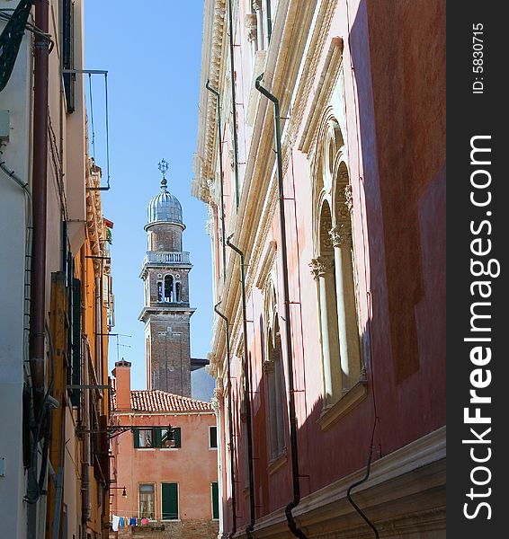Dome of bell tower behind old roofs. A narrow street is in Venice. Linen dries on a rope. Dome of bell tower behind old roofs. A narrow street is in Venice. Linen dries on a rope