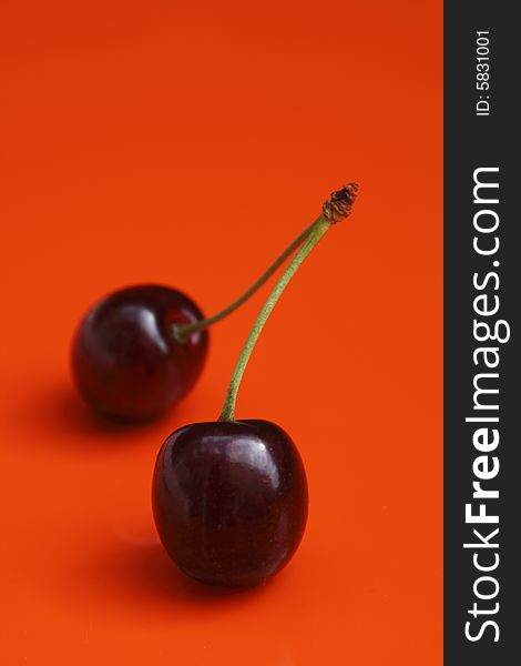 Two cherries on vivid orange background with shadow, shallow DOF