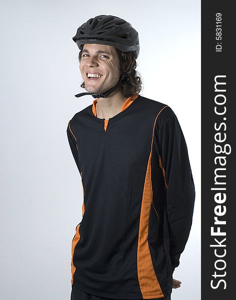 A man stands in a black and orange biking outfit and helmet, smiling at the camera. Vertically framed shot. A man stands in a black and orange biking outfit and helmet, smiling at the camera. Vertically framed shot.