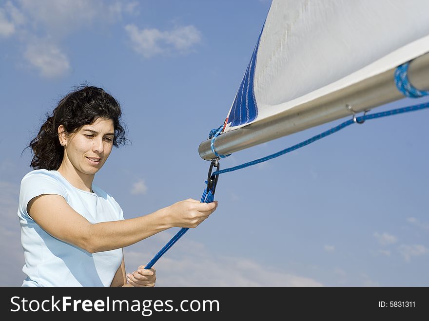 A young woman is fixing the sails on her sailboat.  She is looking away from the camera.  Horizontally framed shot. A young woman is fixing the sails on her sailboat.  She is looking away from the camera.  Horizontally framed shot.