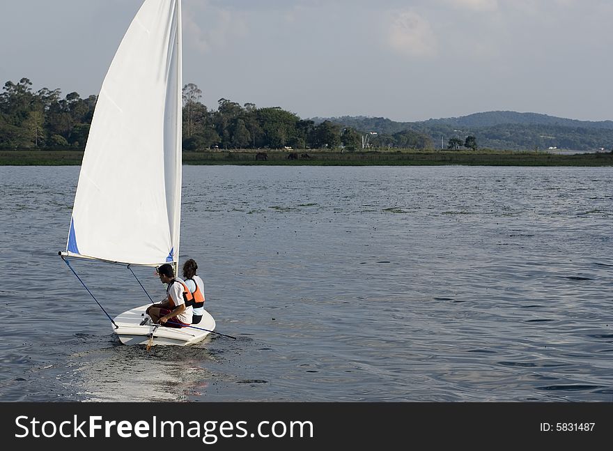 A couple is sailing together on a lake.  They are looking away from the camera.  Horizontally framed shot. A couple is sailing together on a lake.  They are looking away from the camera.  Horizontally framed shot.
