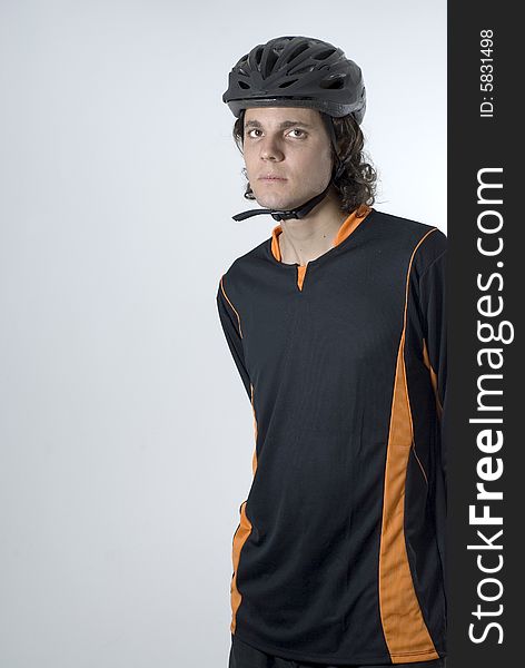 A man, standing, staring at the camera, wears a black and orange shirt with a black helmet. Vertically framed shot. A man, standing, staring at the camera, wears a black and orange shirt with a black helmet. Vertically framed shot.