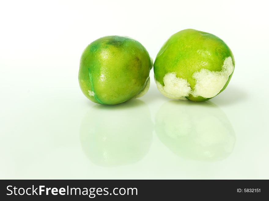 Macro shot of two wasabi coated green peas with reflection.