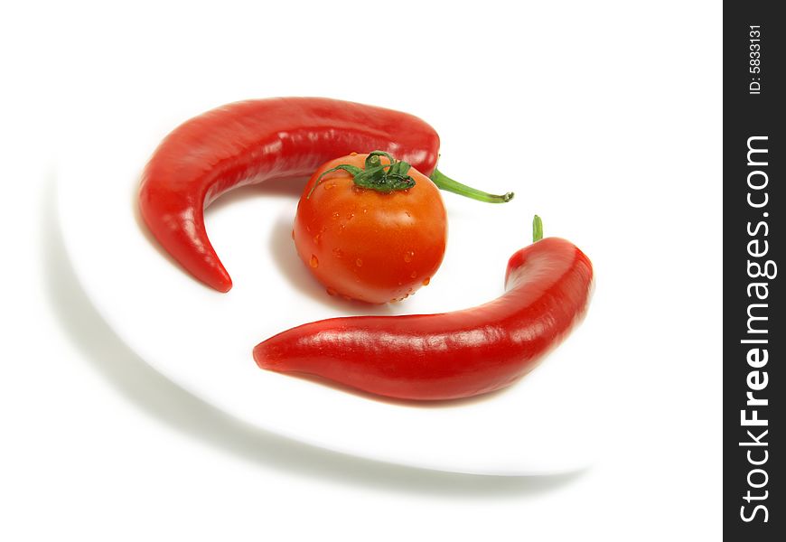 Two fresh chili peppers and a ripe tomato on a white plate and isolated on white background. Two fresh chili peppers and a ripe tomato on a white plate and isolated on white background