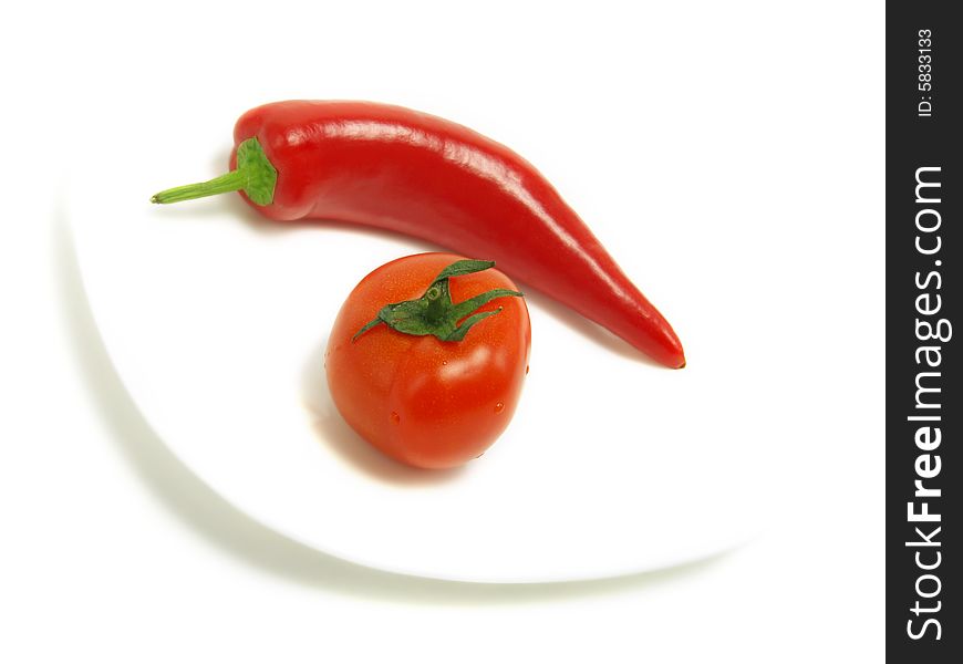 A fresh tomato and a blurred ripe chili pepper on a white plate and isolated on white background. A fresh tomato and a blurred ripe chili pepper on a white plate and isolated on white background