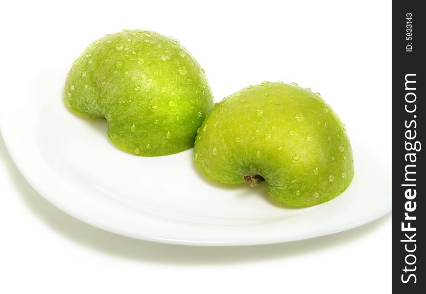 Two half parts of a fresh ripe green apple with water drops on white plate and isolated on white background. Two half parts of a fresh ripe green apple with water drops on white plate and isolated on white background