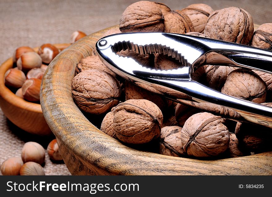 Mixed nuts in bowl with nut cracker on burlap background