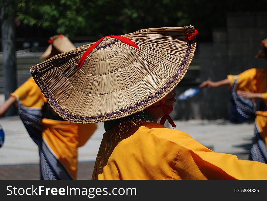 Japanese woman dances obon dance wearing traditional straw hat and yellow yukata. center of image.