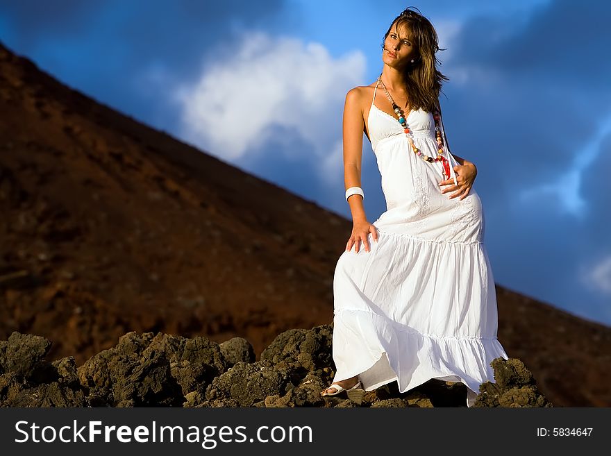 Young model with white dress on volcanic lava rocks. Young model with white dress on volcanic lava rocks