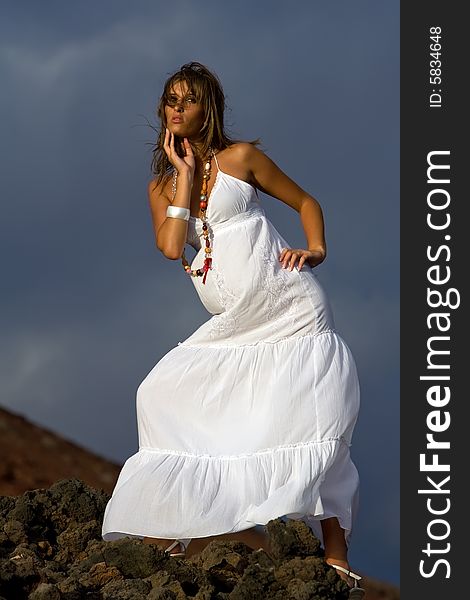 Young model with white dress on volcanic lava rocks. Young model with white dress on volcanic lava rocks