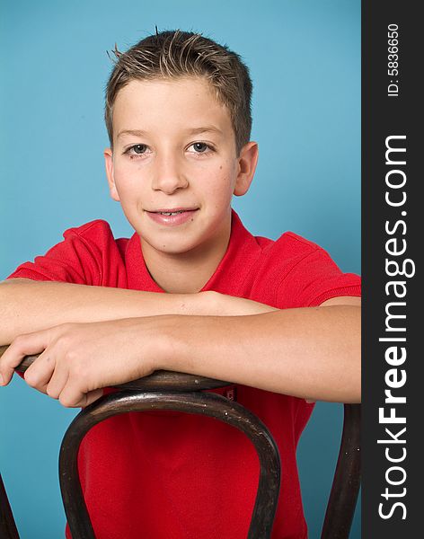 A clean cut young man in a red shirt straddling an old bentwood back chair.