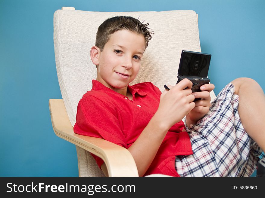 A boy relaxed in a chair holding a video game device. A boy relaxed in a chair holding a video game device.