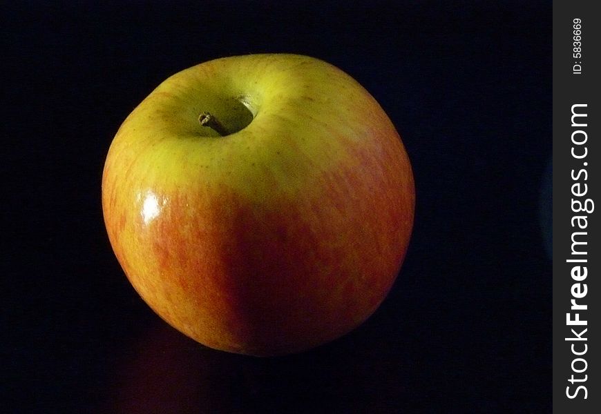 A shiny red-and-green apple against a black background