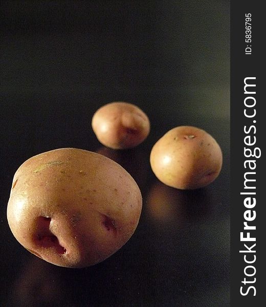 Three red potatoes on a reflective dark surface