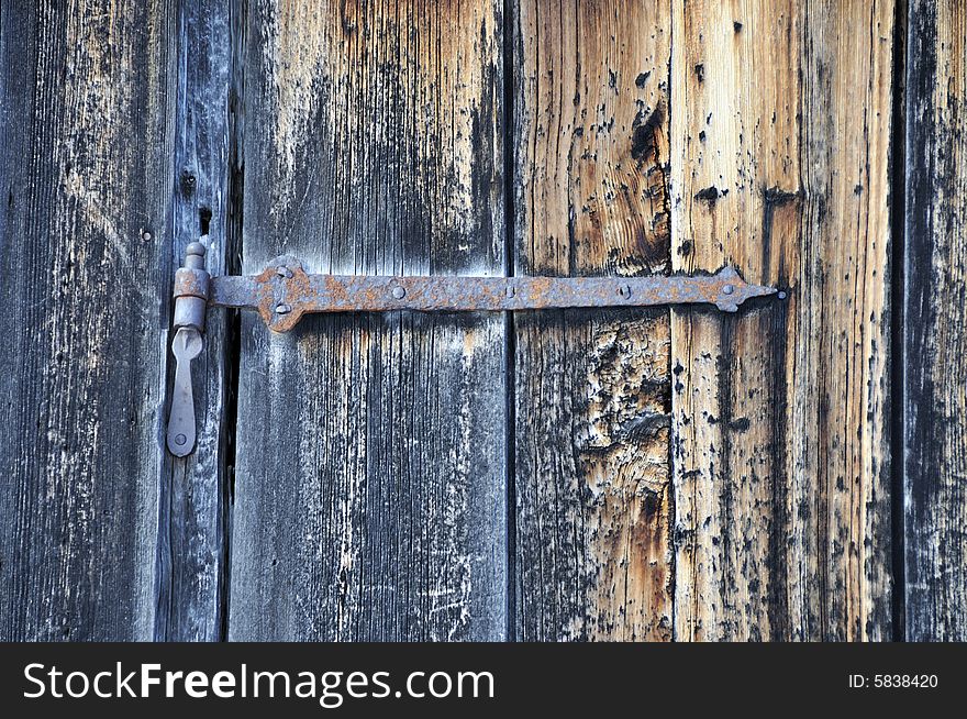 A close up of an old rusted metal hinge on a weathered unpainted door. A close up of an old rusted metal hinge on a weathered unpainted door.