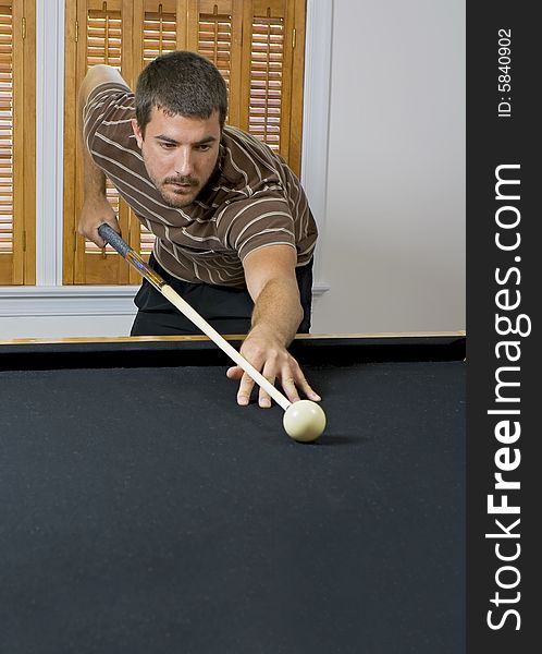 Young man lining up the cue ball, getting ready to break the billiards on the other end of the table. Young man lining up the cue ball, getting ready to break the billiards on the other end of the table.