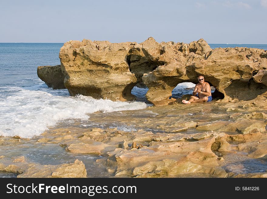 Senior sits in front of carved out arch in Coral Reef Park, Florida bracing for incoming wave.