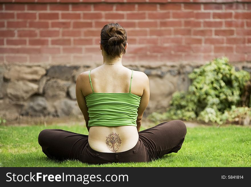 Back of woman with a tattoo sitting on grass. Back of woman with a tattoo sitting on grass