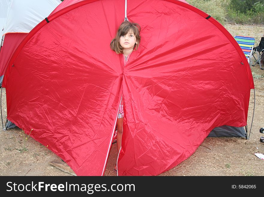 Young girl peeking her head out of a red tent. Young girl peeking her head out of a red tent.