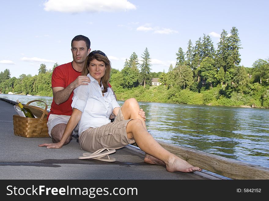 Couple sitting together by a lake with a picnic basket. Horizontally framed photograph. Couple sitting together by a lake with a picnic basket. Horizontally framed photograph