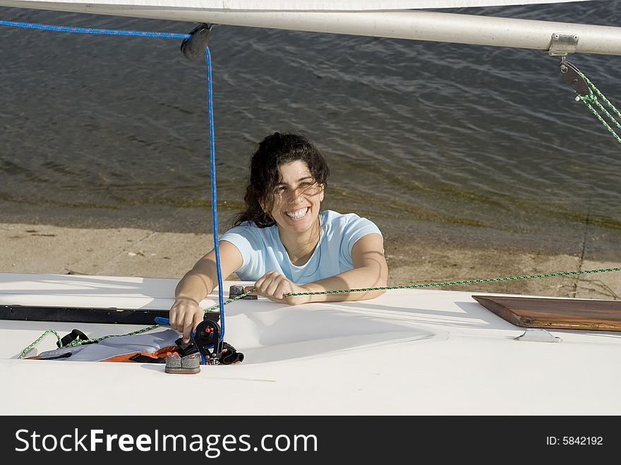 A young woman is  fixing something on her sailboat.  She is smiling and looking away from the camera.  Horizontally framed shot. A young woman is  fixing something on her sailboat.  She is smiling and looking away from the camera.  Horizontally framed shot.