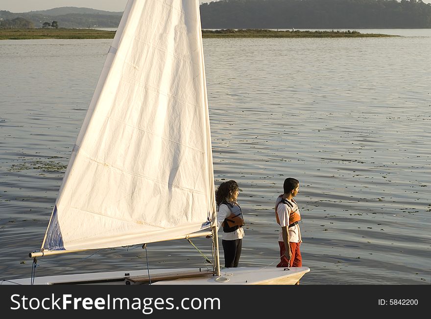 A woman and man are next to a sailboat.  They are looking away from the camera across the lake.  Horizontally framed shot. A woman and man are next to a sailboat.  They are looking away from the camera across the lake.  Horizontally framed shot.