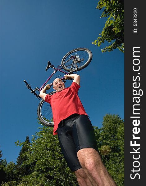 A man lifting a bicycle high over his head on a sunny day, at a park. - vertically framed. A man lifting a bicycle high over his head on a sunny day, at a park. - vertically framed